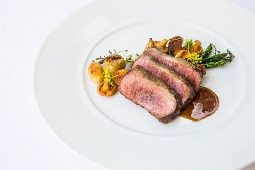 A plate of sliced beef with a rich sauce, accompanied by roasted vegetables and garnished with herbs.