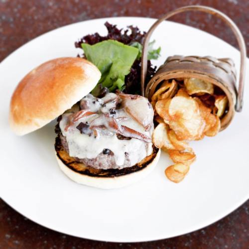 A gourmet burger with melted cheese, topped with bacon, served with a side of crispy potato chips in a small basket.