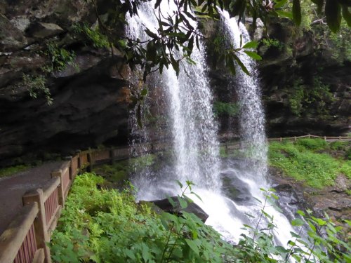 A scenic waterfall cascading over rocks, surrounded by lush greenery and a wooden pathway.