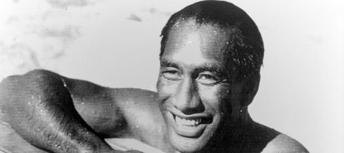 A smiling man with wet skin, resting in water, captured in a black and white photograph.