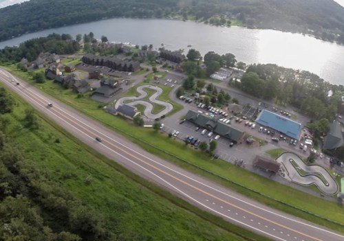 Aerial view of a lakeside area with a winding road, buildings, and recreational facilities near the water.