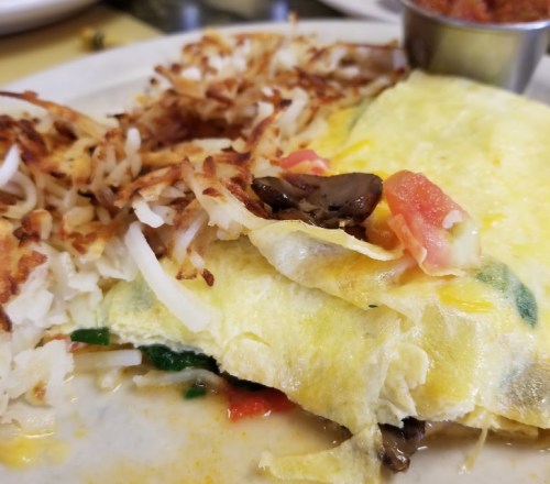 A plate featuring a colorful omelette with vegetables, served alongside crispy hash browns and a small cup of salsa.