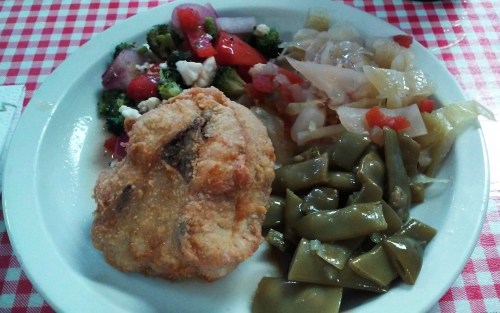 A plate of food featuring a fried item, mixed salad, sautéed cabbage, and green beans on a checkered tablecloth.