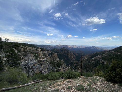 A panoramic view of a mountainous landscape with lush greenery and a blue sky dotted with clouds.