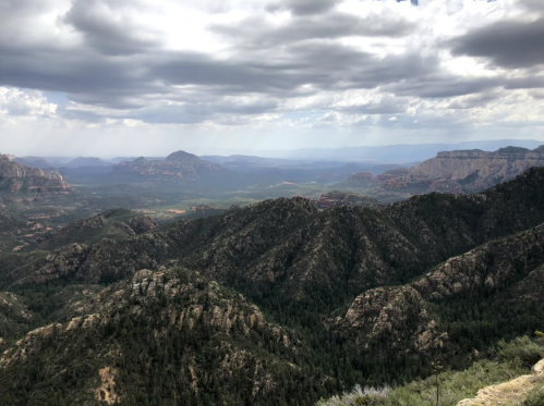 A panoramic view of rugged mountains and valleys under a cloudy sky, showcasing lush greenery and distant peaks.