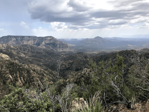 A panoramic view of rugged mountains and valleys under a cloudy sky, showcasing lush greenery in the foreground.
