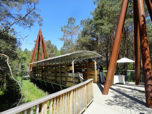 A wooden bridge with a covered section, surrounded by trees and a clear blue sky.