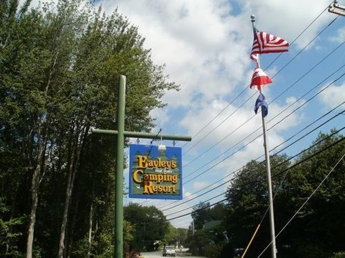 Sign for Paquley's Camping Resort with flags and trees in the background under a partly cloudy sky.