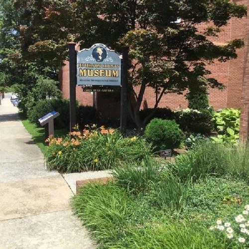 Sign for Jefferson County Museum surrounded by greenery and flowers, with a brick building in the background.