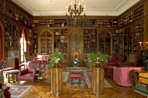 A grand library with wooden shelves filled with books, elegant furniture, and decorative plants in a classic setting.