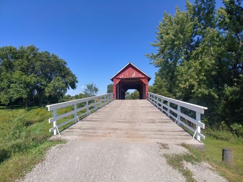 A red covered bridge with a wooden walkway, surrounded by green trees and a clear blue sky.