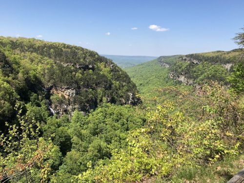 A scenic view of lush green valleys and cliffs under a clear blue sky, with distant mountains visible.
