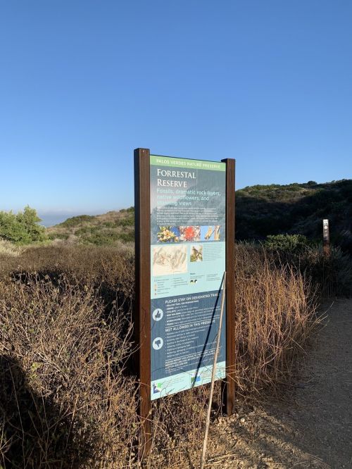 Sign for Forresteral Reserve with information about local wildlife and nature trails, surrounded by shrubs and clear blue sky.
