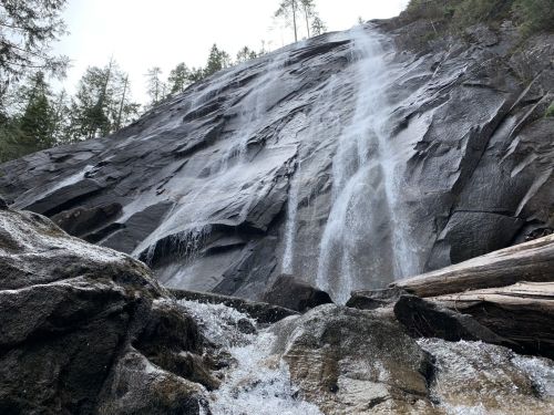 A cascading waterfall flows down a rocky cliff, surrounded by trees and a misty atmosphere.