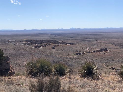 A panoramic view of a vast desert landscape with distant mountains and sparse vegetation under a clear blue sky.