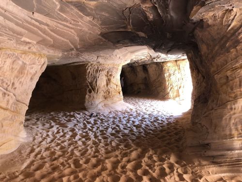 A sandy cave interior with textured rock walls and light streaming in from an opening.