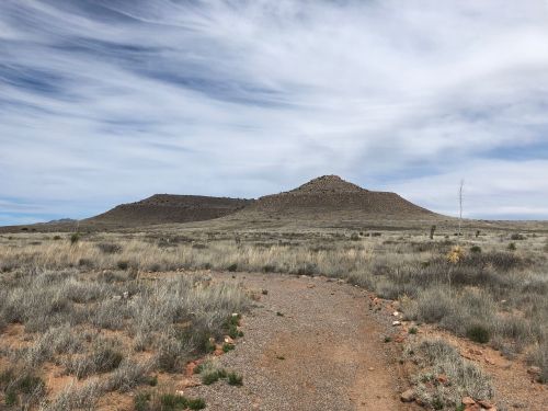 A gravel path leads through a grassy landscape towards two low, rocky hills under a cloudy sky.