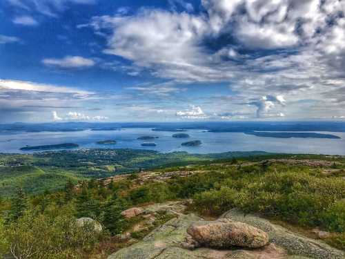 A panoramic view of a lake surrounded by islands, with lush greenery and a cloudy blue sky above.