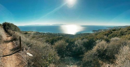 A panoramic view of a coastal landscape with sparkling water, distant islands, and lush greenery under a clear blue sky.