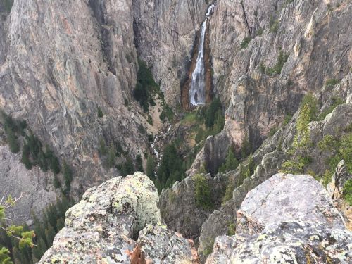 A scenic view of a waterfall cascading down rocky cliffs, surrounded by lush greenery and rugged terrain.