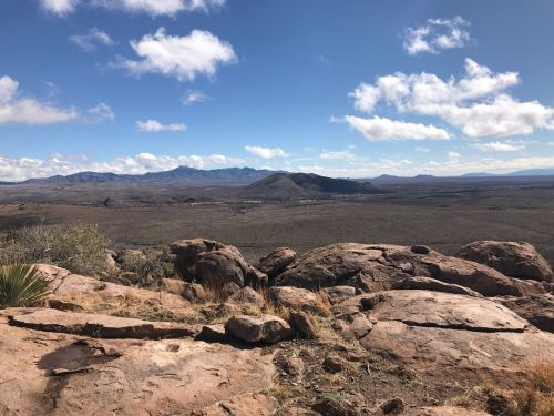 A panoramic view of a rocky landscape with mountains and a blue sky dotted with clouds.