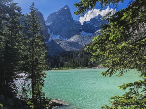A serene turquoise lake surrounded by lush green trees and towering mountains under a clear blue sky.