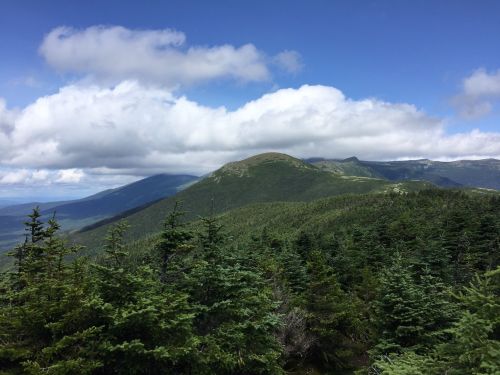 A panoramic view of green mountains under a blue sky with clouds, showcasing a lush, forested landscape.