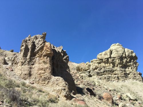 Rocky formations rise against a clear blue sky, showcasing textured cliffs and sparse vegetation below.