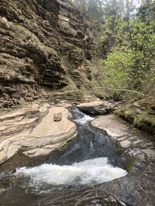 A serene river flows through rocky terrain, surrounded by lush greenery and steep cliffs.