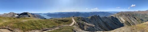 A panoramic view of mountains and valleys under a clear blue sky, with a winding path leading through the landscape.