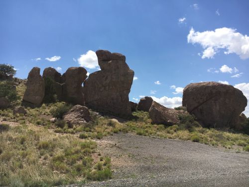 A cluster of large boulders on a grassy area under a blue sky with scattered clouds.