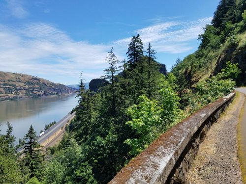 A scenic view of a river surrounded by lush greenery and hills under a clear blue sky.
