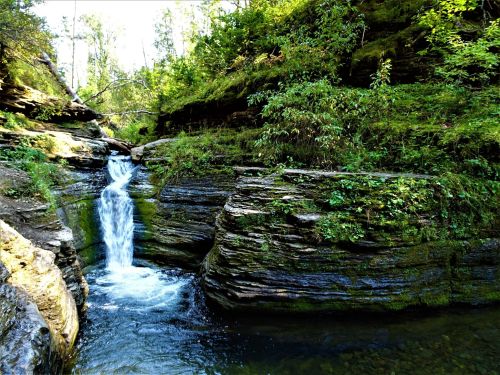 A serene waterfall cascades over rocky cliffs, surrounded by lush greenery and trees in a peaceful natural setting.