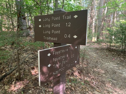 Trail signs in a wooded area, indicating directions and distances to Long Point Trail, Fayetteville Trail, and Town Park.