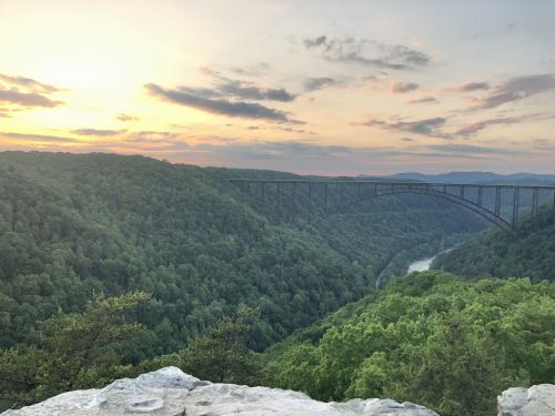 A scenic view of a bridge spanning a lush green valley at sunset, with clouds and a river below.