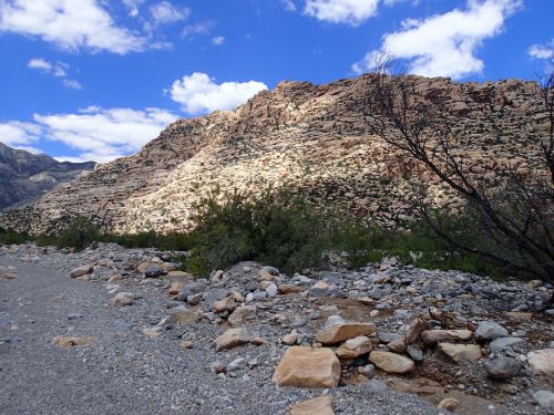 A rocky landscape with a mountain in the background, under a blue sky with scattered clouds.