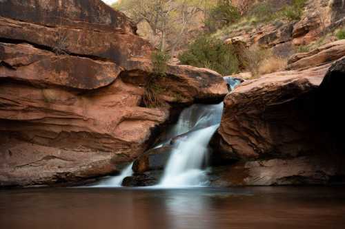 A serene waterfall cascading over rocky cliffs into a calm pool, surrounded by lush greenery and rugged terrain.