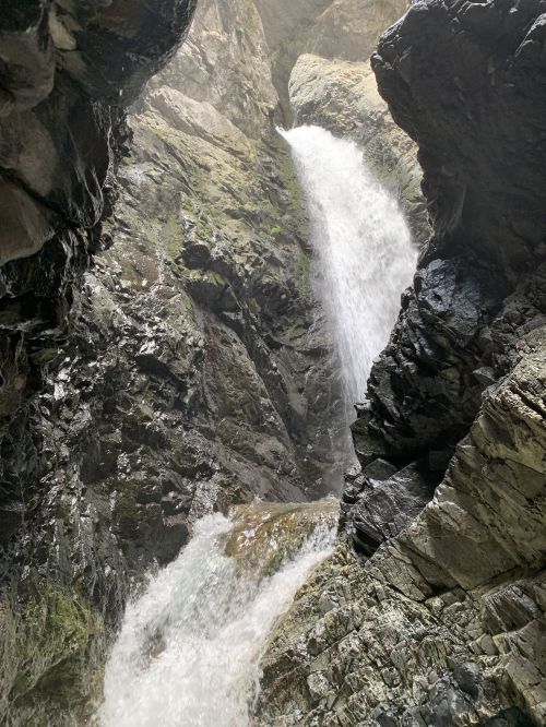 A waterfall cascading between rocky cliffs, surrounded by moss and wet stone, creating a misty atmosphere.