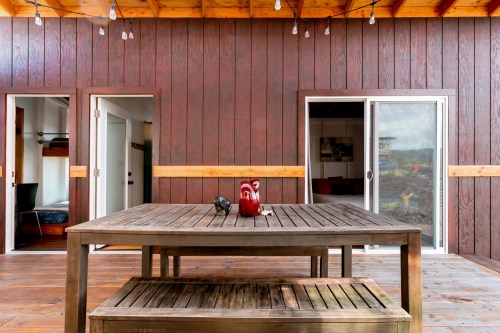 A wooden table with decor sits in a cozy outdoor space, flanked by two doors and warm string lights overhead.