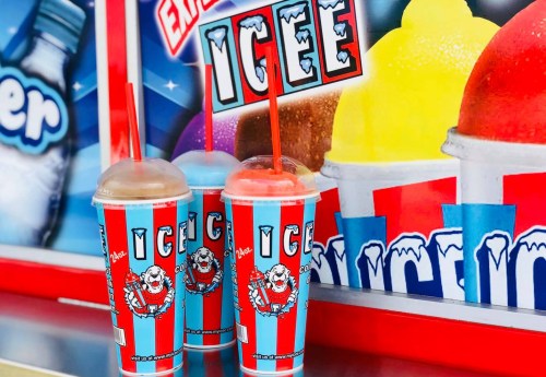 Two colorful ICEE cups with straws sit in front of a vibrant ICEE advertisement featuring various flavors.