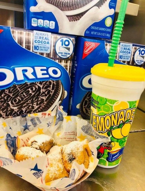 A colorful cup of lemonade next to a basket of powdered sugar-dusted treats, with Oreo boxes in the background.