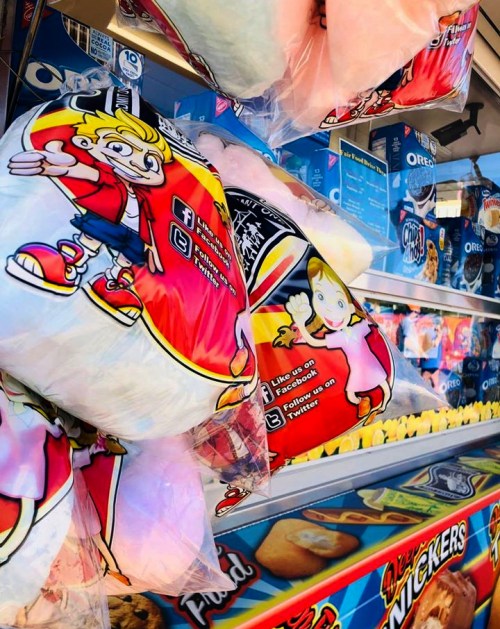 Colorful cotton candy bags with cartoon characters, surrounded by various snacks and treats in a vending display.