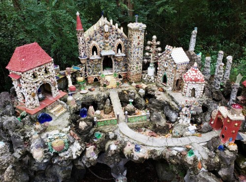 A whimsical miniature village made of colorful stones and shells, surrounded by greenery.