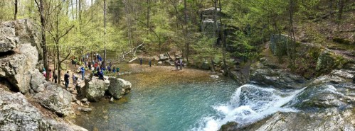 A scenic waterfall surrounded by lush greenery, with a group of people gathered near the water's edge.
