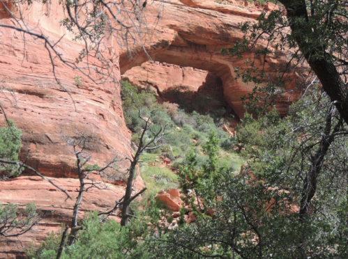 A natural rock arch surrounded by red sandstone cliffs and green vegetation.
