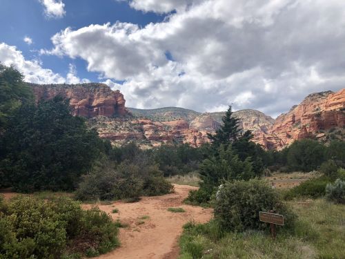 A scenic view of red rock formations and green vegetation under a partly cloudy sky.