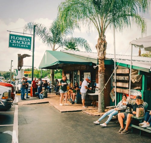 A busy outdoor dining area at Florida Cracker Kitchen, with people sitting and enjoying the atmosphere under palm trees.