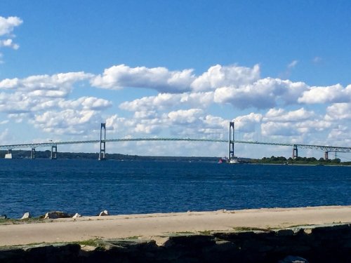 A bridge spans across a calm body of water under a blue sky with fluffy clouds.