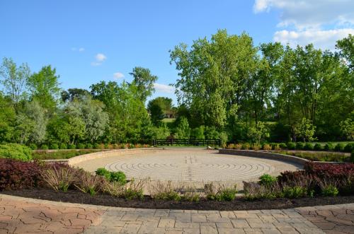 A circular stone labyrinth surrounded by lush greenery and colorful plants under a clear blue sky.