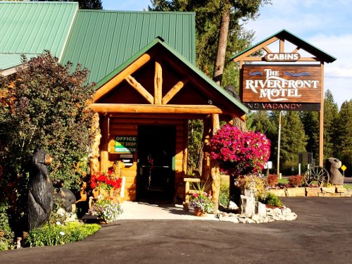 A rustic motel entrance with a wooden facade, colorful flowers, and a sign reading "The Riverfront Motel - No Vacancy."